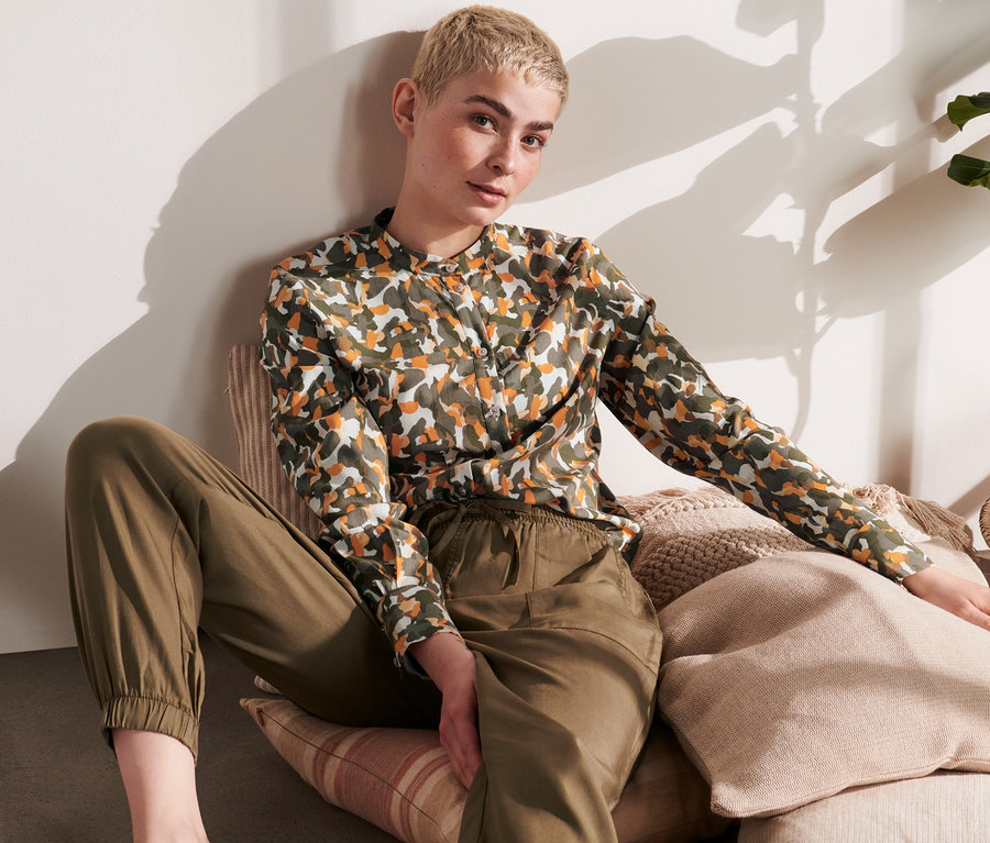 Frau sitzt auf Kissen und trägt eine Hemdbluse mit Print.