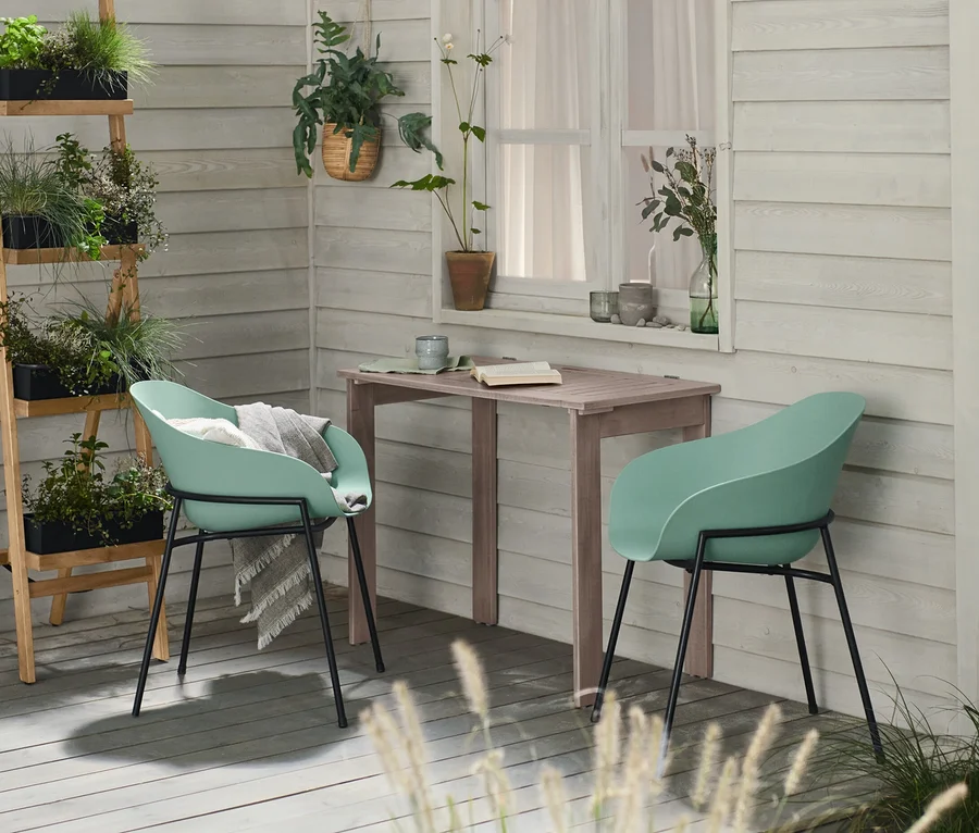 Ein klappbarer Gartentisch »Leira« steht zwischen zwei mintfarbenen Schalenstühlen auf einer Holzterrasse. Links eine zusammenklappbare schwarze Pflanzleiter mit Pflanzen.