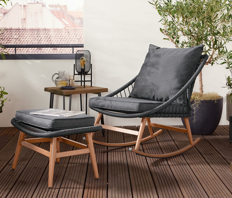 Schaukelsessel mit Fußhocker steht auf einer Terrasse neben einem Tisch.