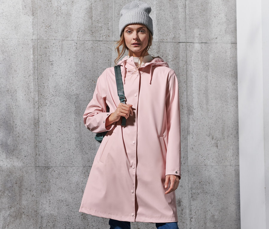Frau trägt rosa Regenparka, Jeans und weiße Stiefel.