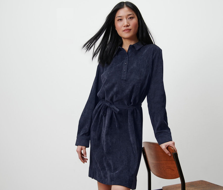 Frau posiert in einem Cordkleid und lehnt sich an einen Stuhl.