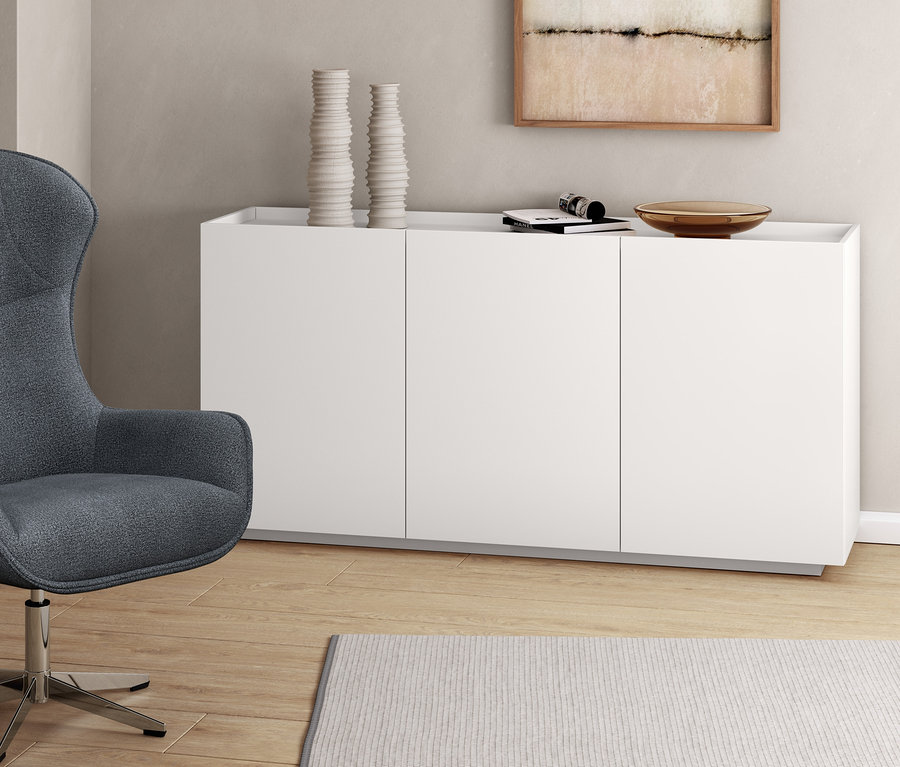 Grauer Sessel mit Drehfunktion neben weißem Sideboard.