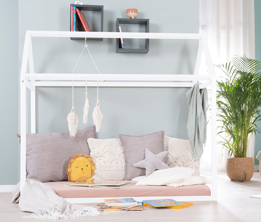 Weißes roba Hausbett, ca. 70 x 140 cm, mit Kissen und Spielzeug drinnen, Bücher auf dem Boden, Pflanze in der Ecke.