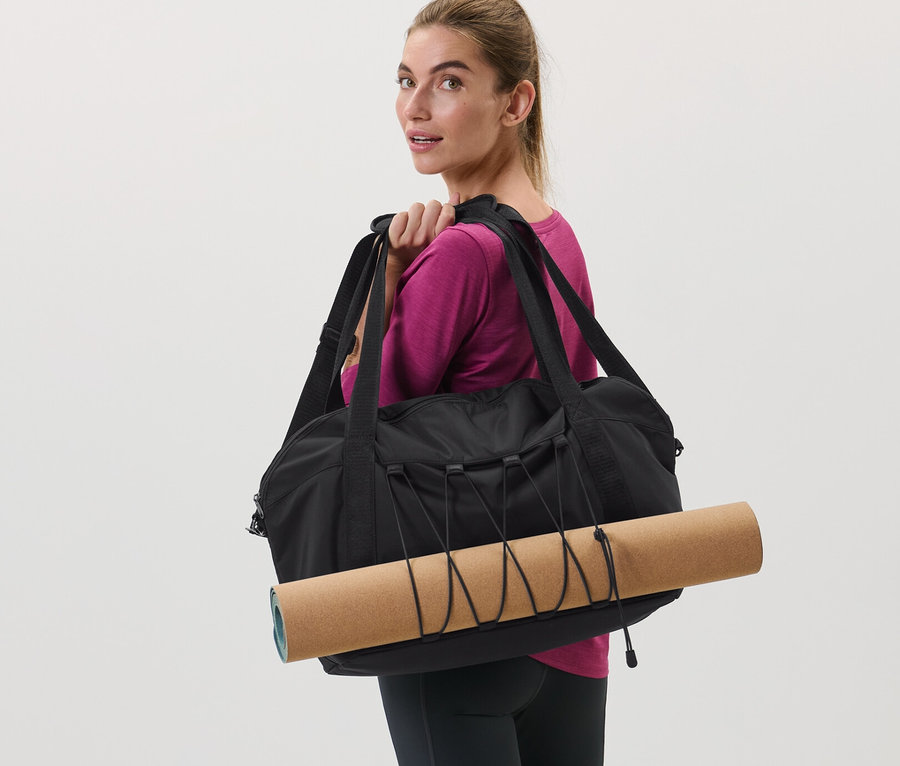 Frau trägt schwarze Sporttasche und Yogamatte über der Schulter.