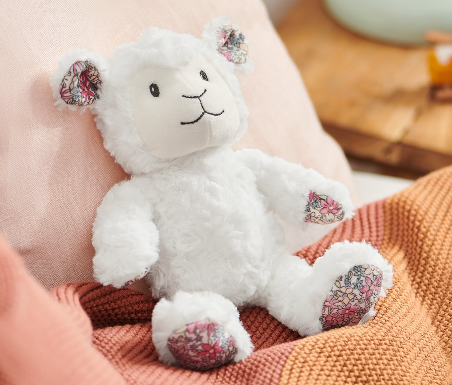 Ein Plüsch-Schaf liegt auf einem Bett mit rosa Kissen und einer orangefarbenen Decke.