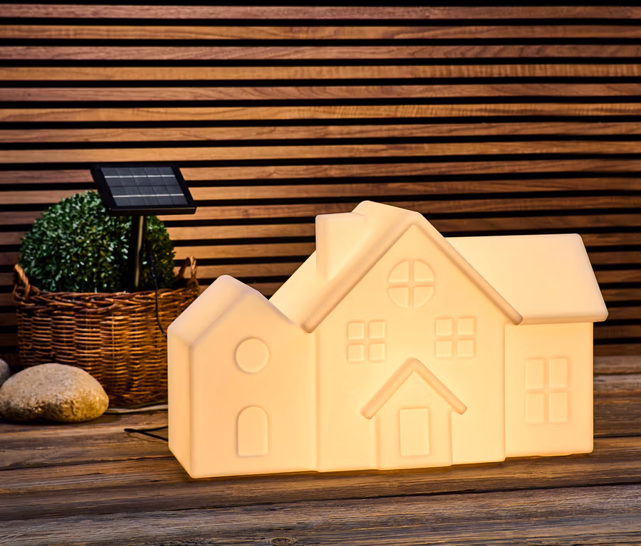Eine Solar-Outdoorleuchte in Hausform steht auf einer Holzfläche.