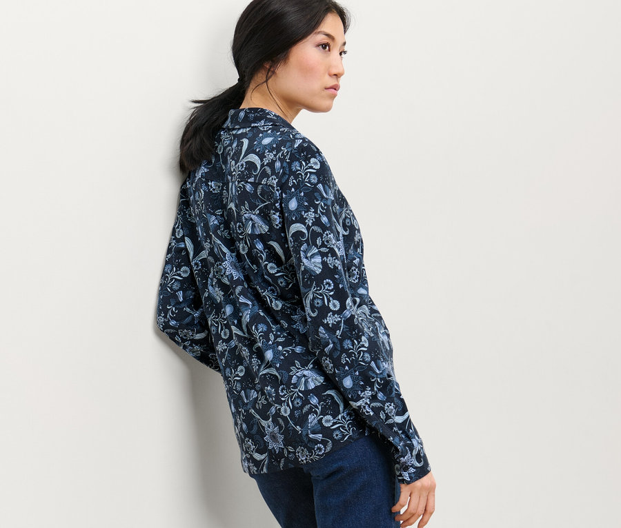 Frau posiert in einem bedruckten Blusenshirt mit Knopfleiste und Jeans.