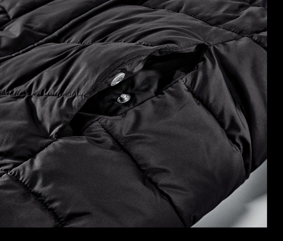 Detailansicht eines schwarzen Steppmantels mit Kapuze und Druckknöpfen.