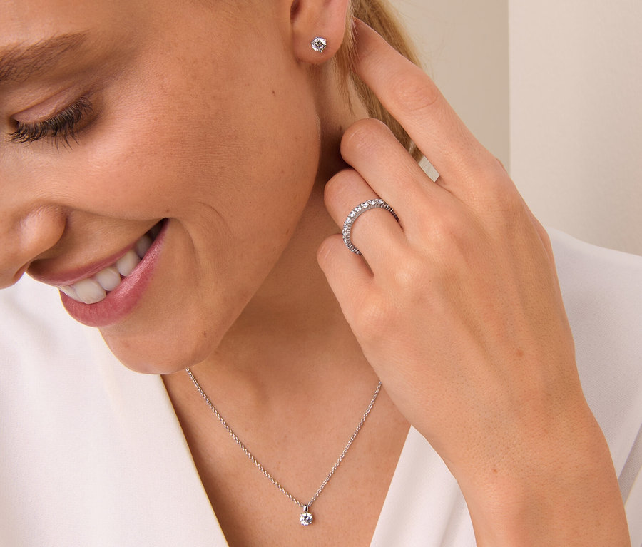 Frau lächelt und berührt ihr Ohr, sie trägt einen 925 Silber Ring Memory, eine 925 Silber Kette Solitär und 925 Silber Ohrstecker Solitär.