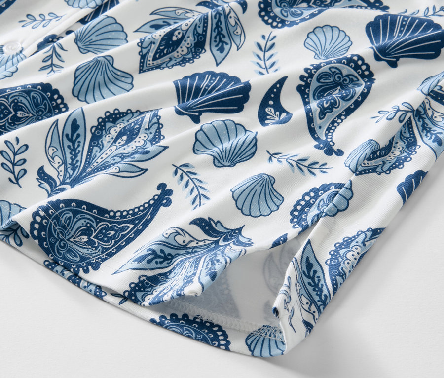 Detailansicht eines Nachthemds mit blauem Muschel- und Paisleymuster auf weißem Grund.
