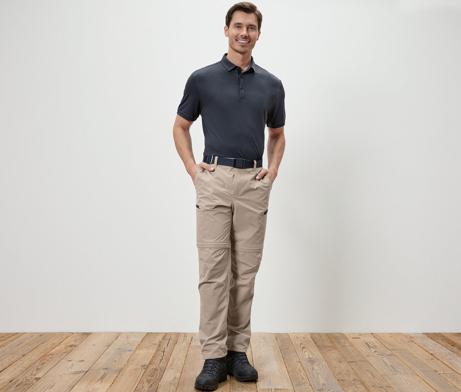 Ein Mann steht mit den Händen in den Taschen einer beige 2-in-1-Funktionshose.