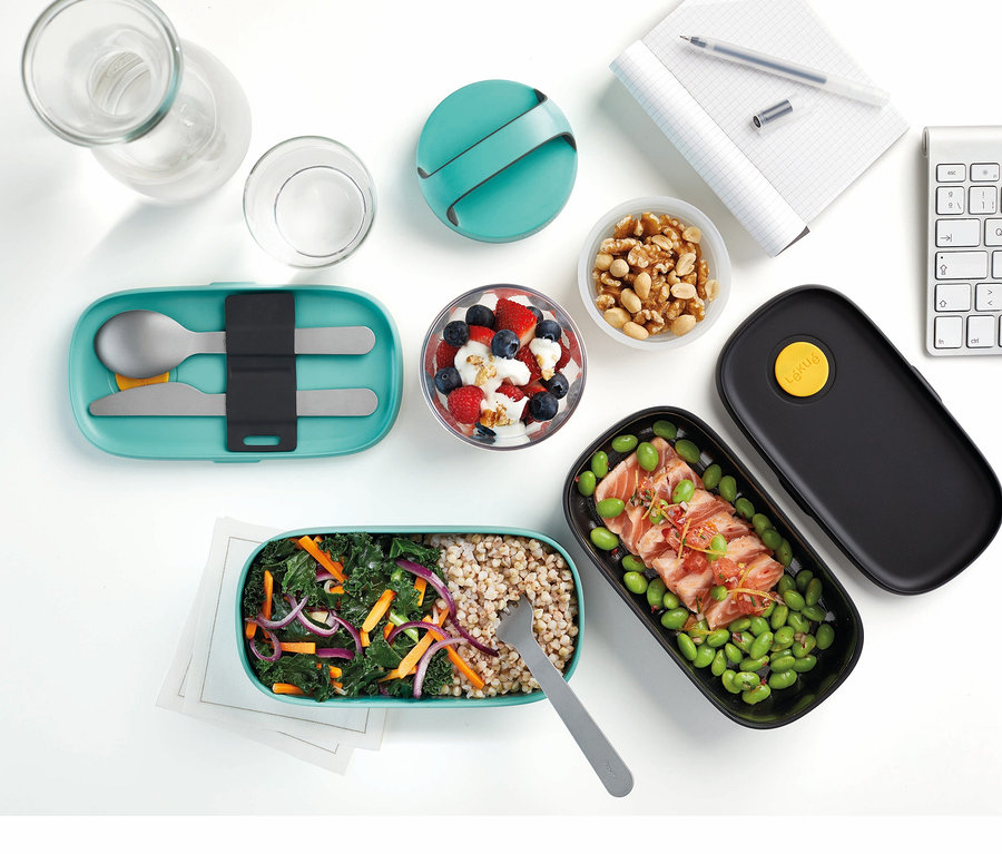 Lunch-Box-Set mit Besteck und andere Behälter mit Lebensmitteln auf einem weißen Tisch.