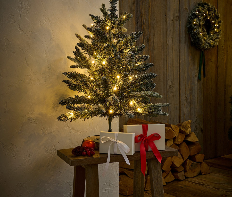Beleuchteter Weihnachtsbaum auf einem Holzschemel mit Geschenken und Dekorationen.