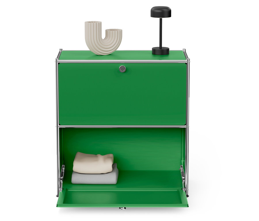 Grüner Schrank mit geöffneten Türen, darauf eine beige Vase und eine schwarze Lampe.