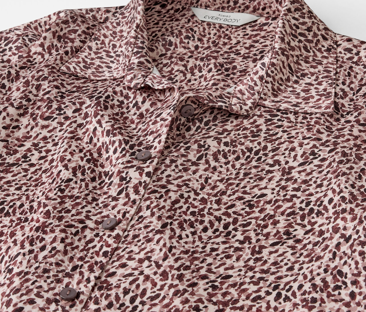 Detailaufnahme eines braun-cremefarbenen Hemdes mit Knöpfen und Muster.