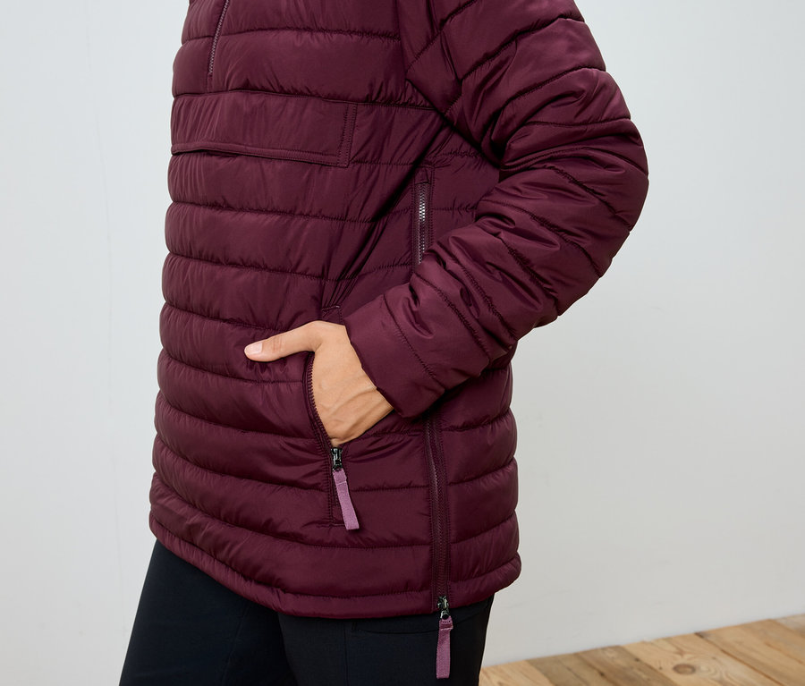 Frau mit Hand in der Tasche einer weinroten Steppjacke.