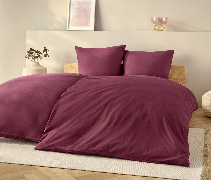Ein lila Bettwäsche-Set auf einem Bett mit einem weißen Teppich.