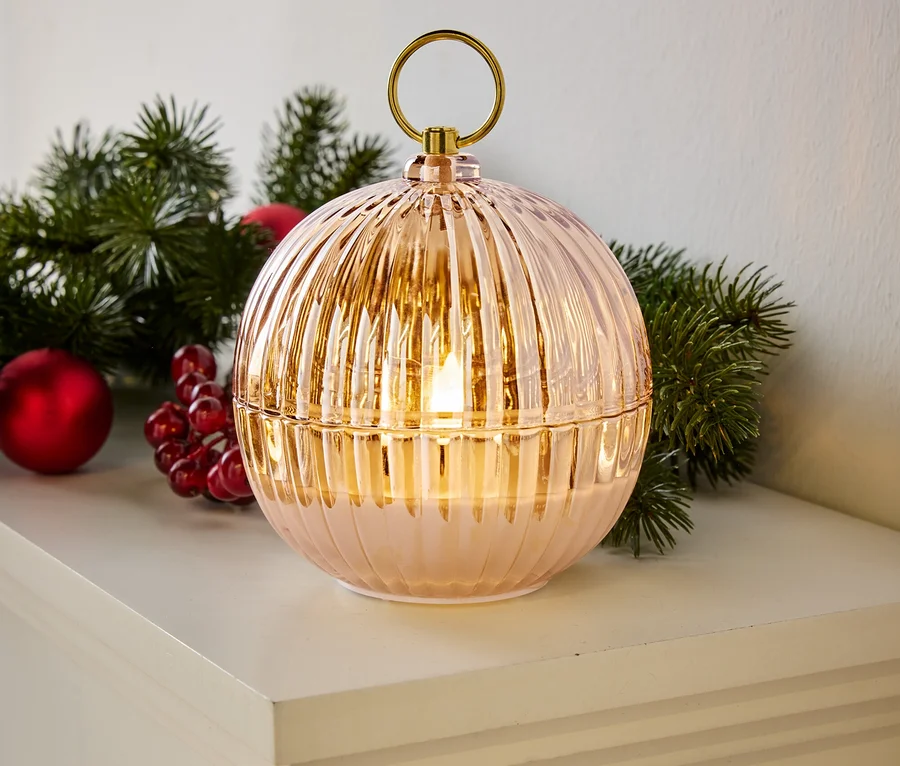 Dekorative Kugellampe mit geriffelter Oberfläche, goldenem Griff und LED-Licht, platziert auf einem weißen Regal neben Weihnachtsdekoration.