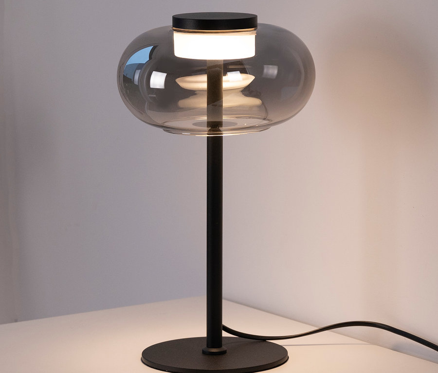 Eine graue Tischleuchte mit Glasschirm steht auf einem weißen Tisch.