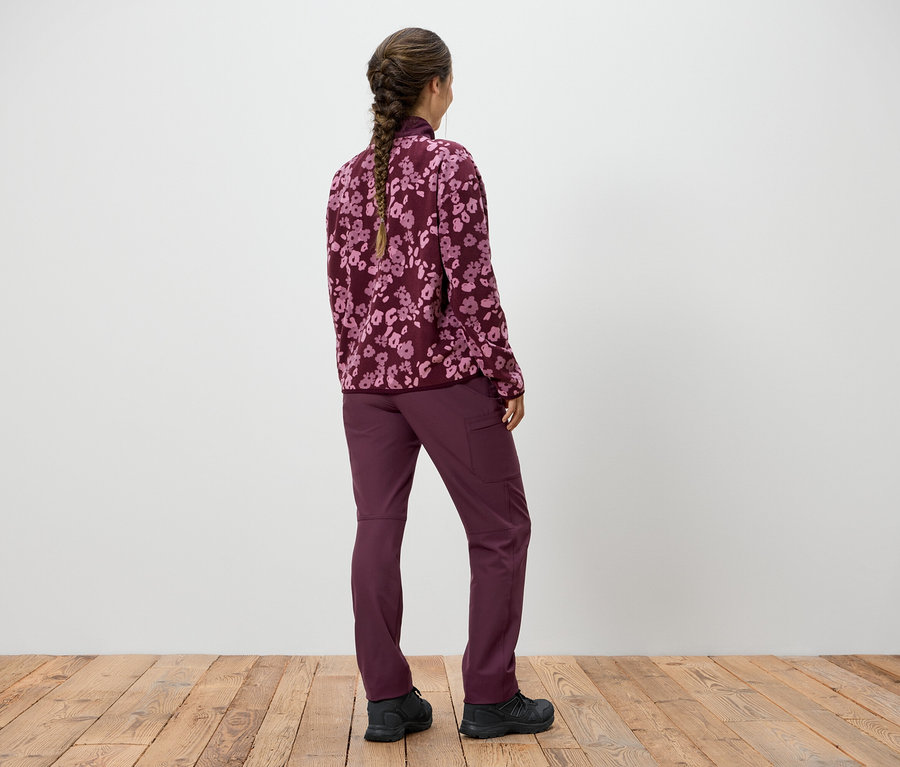 Frau mit Zopf steht mit dem Rücken zur Kamera und trägt ein violettes Sweatshirt mit Blumenmuster und eine violette Hose.