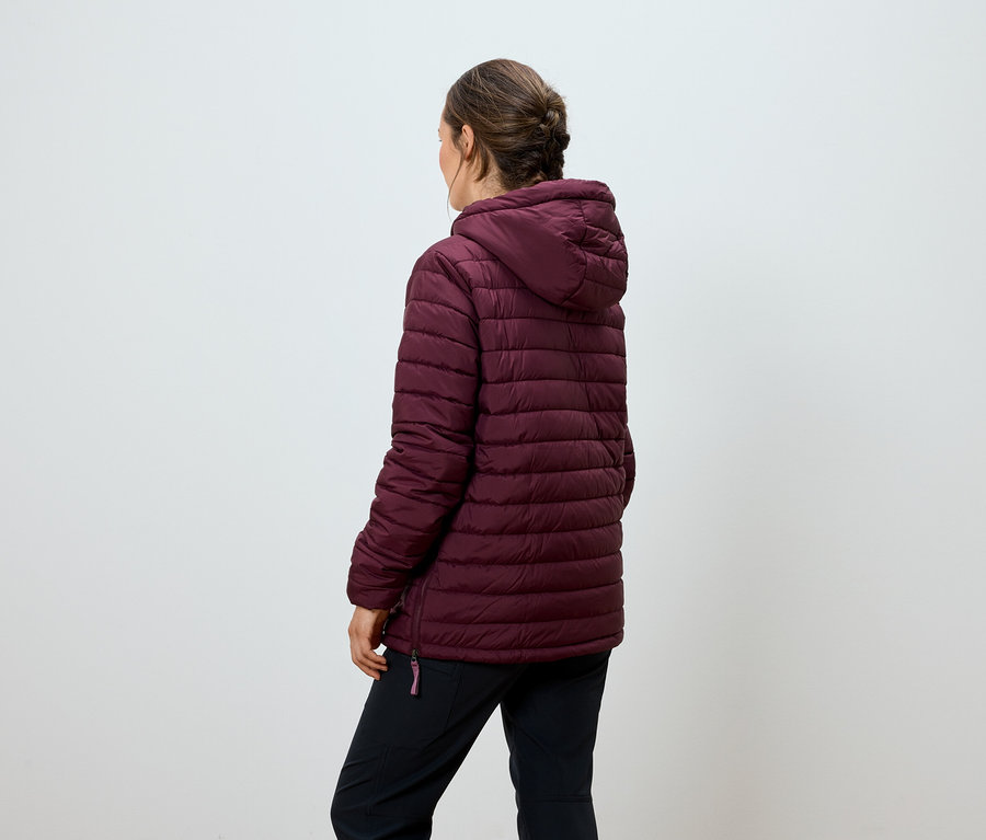 Frau steht mit dem Rücken zur Kamera und trägt eine weinrote Steppjacke mit Kapuze und eine schwarze Hose.