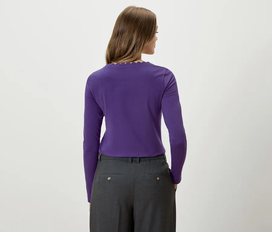 Frau mit dem Rücken zur Kamera trägt ein lila Langarmshirt und eine graue Hose.