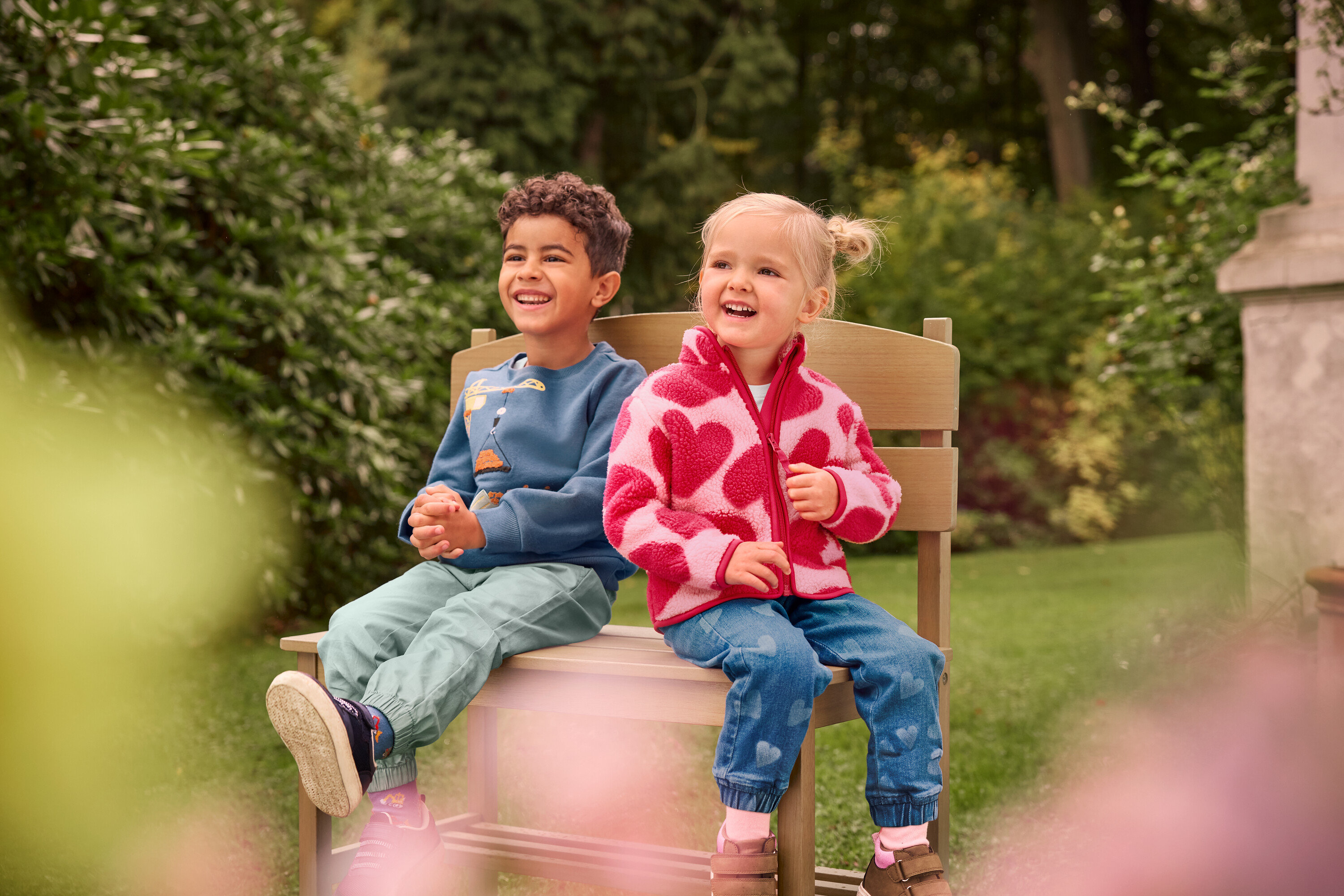 Ein Junge und ein Mädchen sitzen lachend auf einer kleinen Gartenbank mit Ablage.