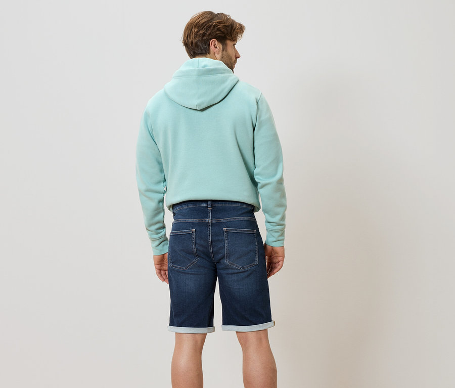 Rückansicht eines Mannes mit hellblauem Hoodie und Jeansshorts.