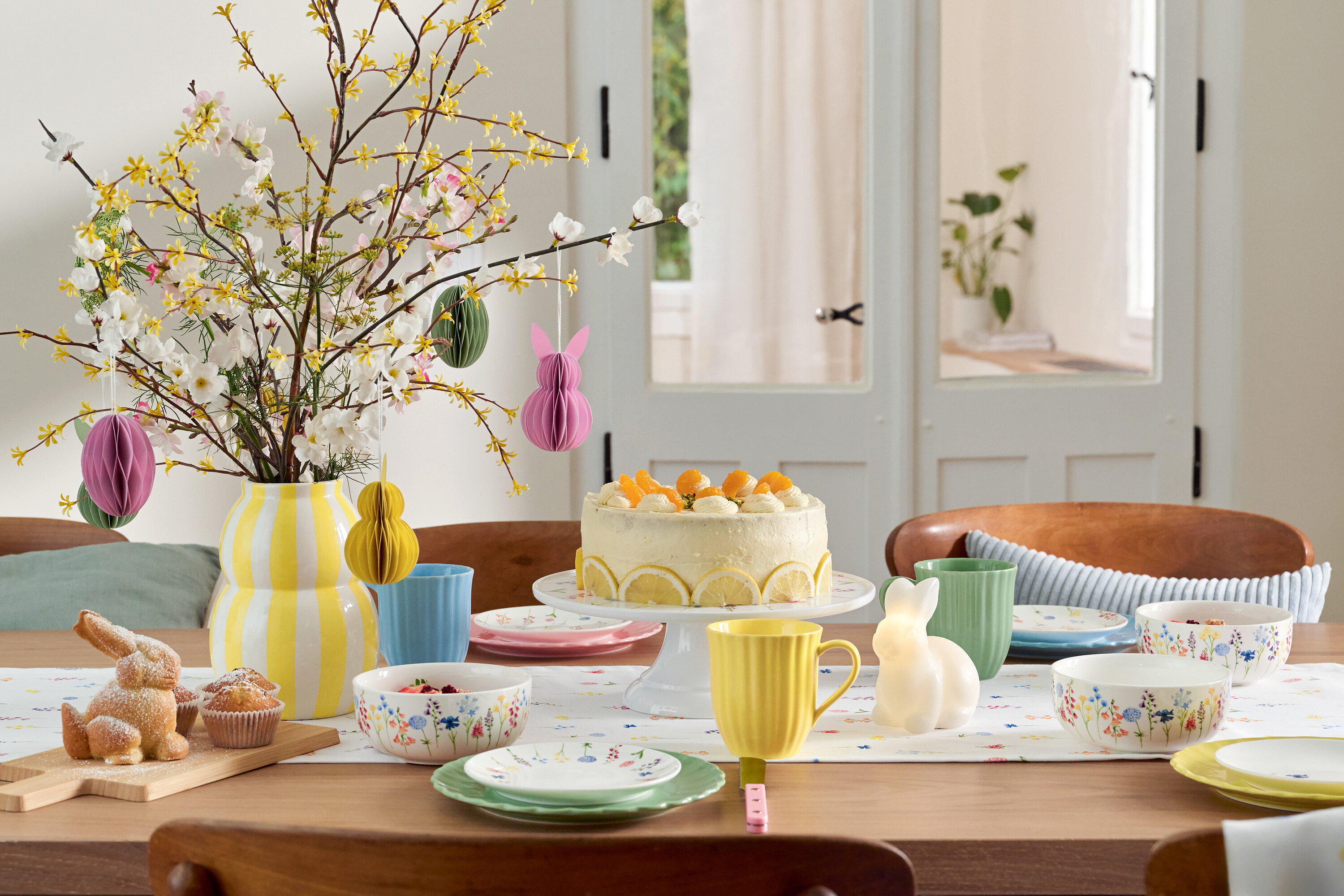 Esstisch mit Osterdekoration, Kuchen, Geschirr und Blumenvase.