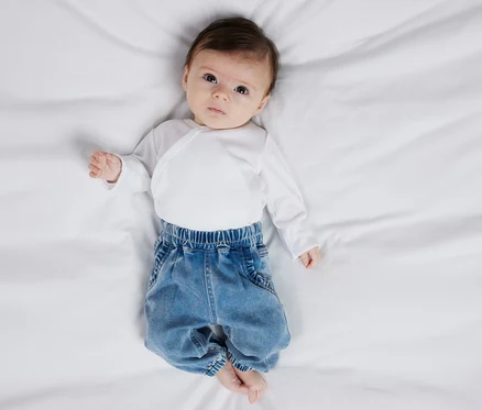 Baby liegt auf dem Rücken und trägt eine weiße Wickelbluse und eine NAME IT Baby-Jeans.