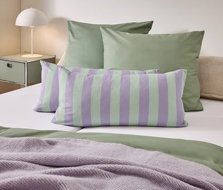 Ein Bett mit grüner Bettwäsche, gestreiften Kissen und einer lila Decke.