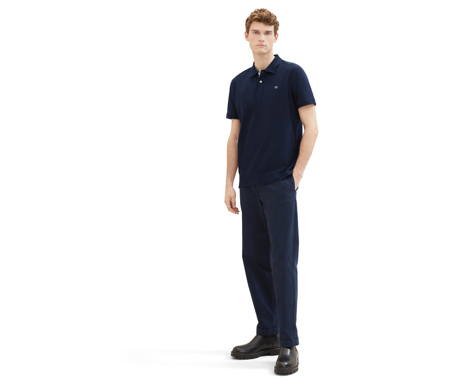 Mann in Hose und Tom Tailor Piqué Poloshirt in Sky Captain Blue, mit einer Hand in der Hosentasche.