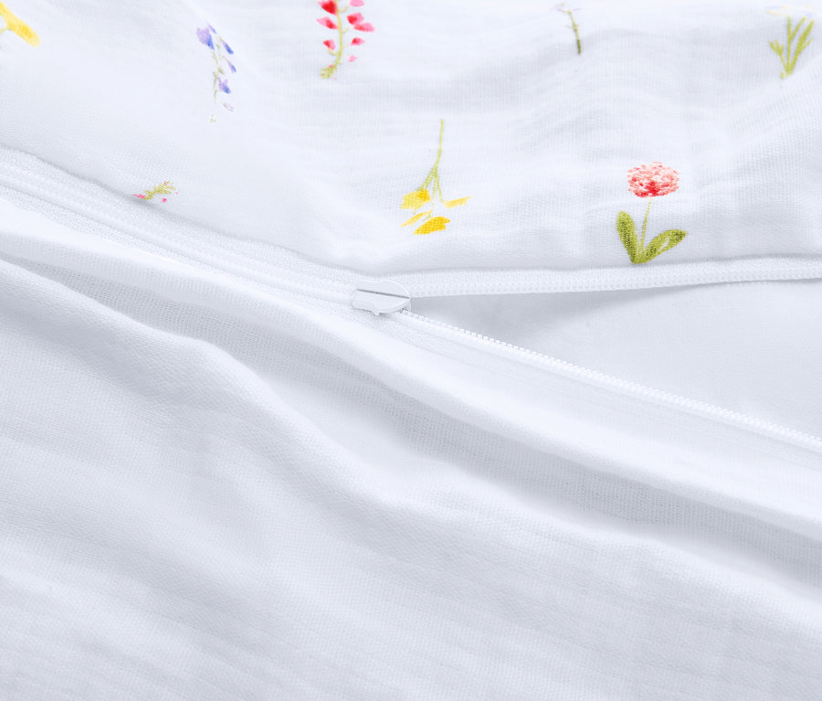 Detailansicht eines teilweise geöffneten, weißen Schlafsacks mit Reißverschluss und Blumenmuster.