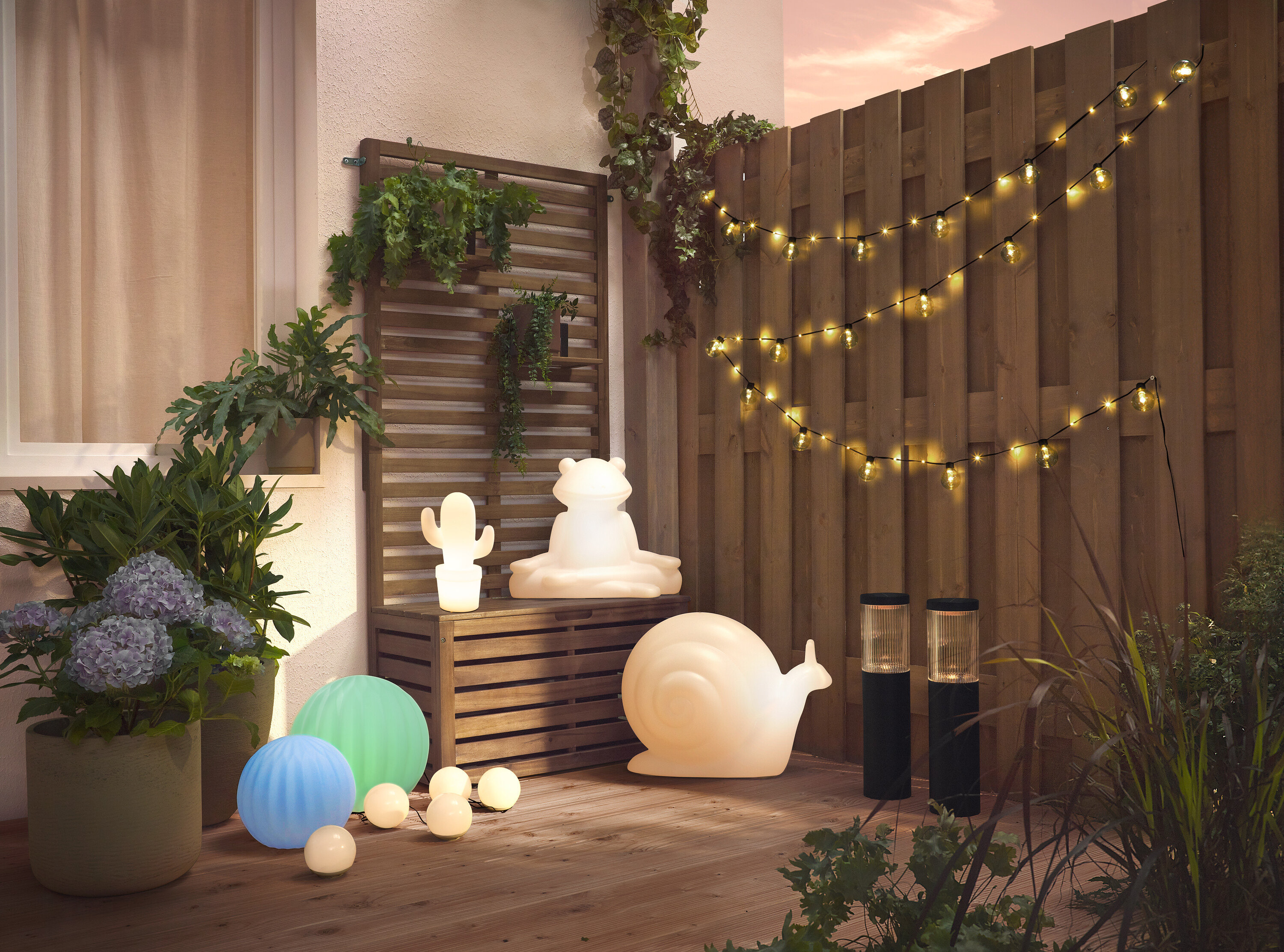 Beleuchtete Solar-Leuchte »Frosch« sitzt auf einer Holzbank neben einer Solar-Leuchte »Schnecke«.