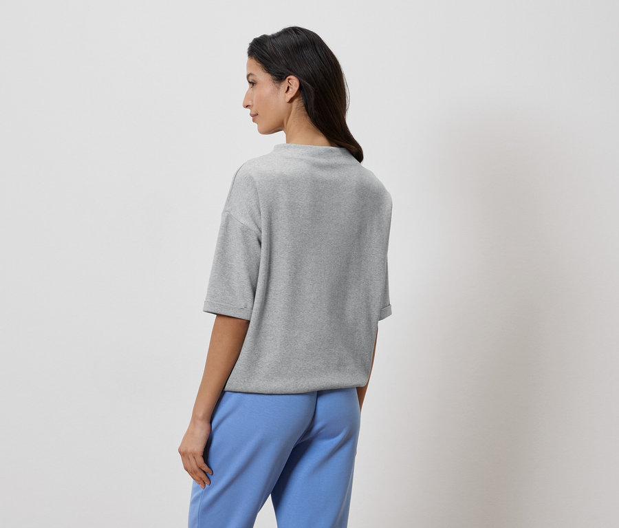 Frau von hinten, trägt graues T-Shirt und blaue Hose.