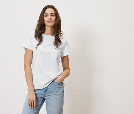 Frau mit braunen Haaren trägt ein weißes T-Shirt und Jeans