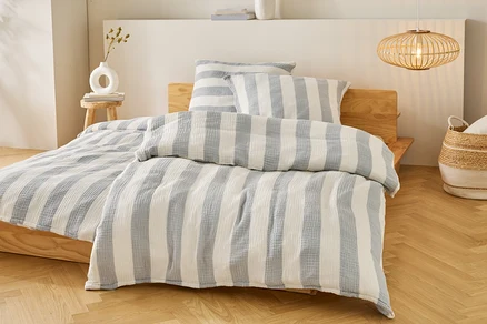 Bett mit blau-weiß gestreifter Bettwäsche und Kissen auf einem Holzbettgestell. Eine Lampe hängt über dem Bett.