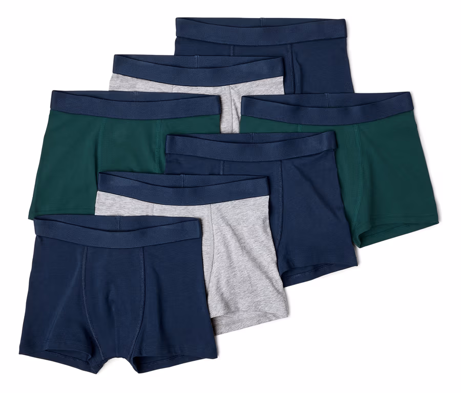 Sieben Boxershorts in Marineblau, Grün und Grau liegen übereinander.