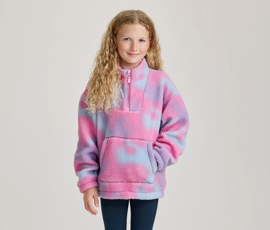 Lächelndes Mädchen mit blonden Locken trägt einen pink-lila-blauen Tie-Dye-Fleece-Pullover mit Reißverschluss und Bauchtasche.