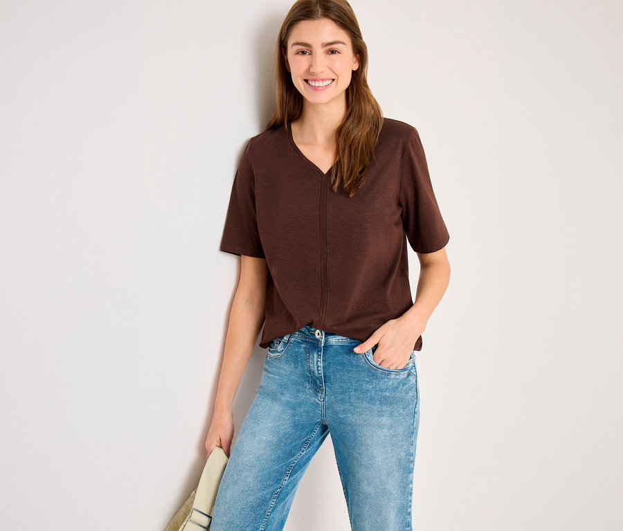 Frau trägt ein braunes CECIL Tunika-Shirt mit V-Ausschnitt und helle Jeans, lächelt in die Kamera.