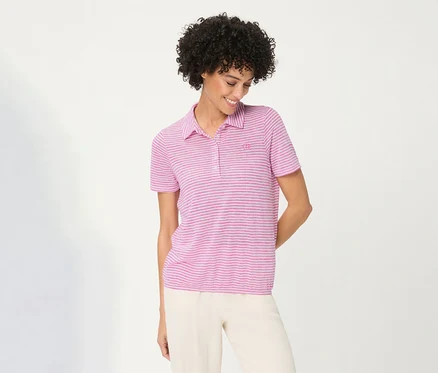 Lächelnde Frau mit lockigem Haar trägt ein pink gestreiftes Olsen Poloshirt und helle Hose, blickt nach unten.