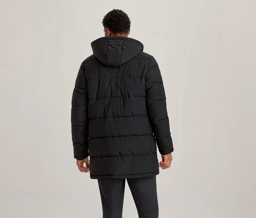 Person von hinten, trägt eine schwarze, wattierte Jacke mit Kapuze, die bis zur Mitte des Oberschenkels reicht.