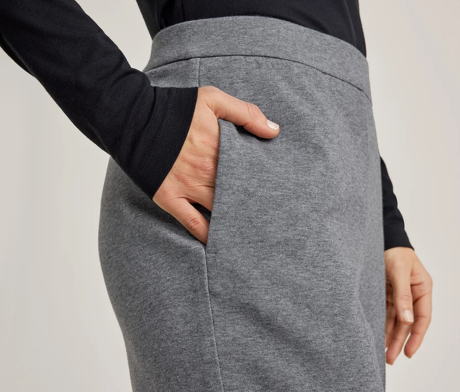 Nahaufnahme einer Person in einem schwarzen Langarmshirt und einer grauen Hose, die rechte Hand in der Hosentasche.