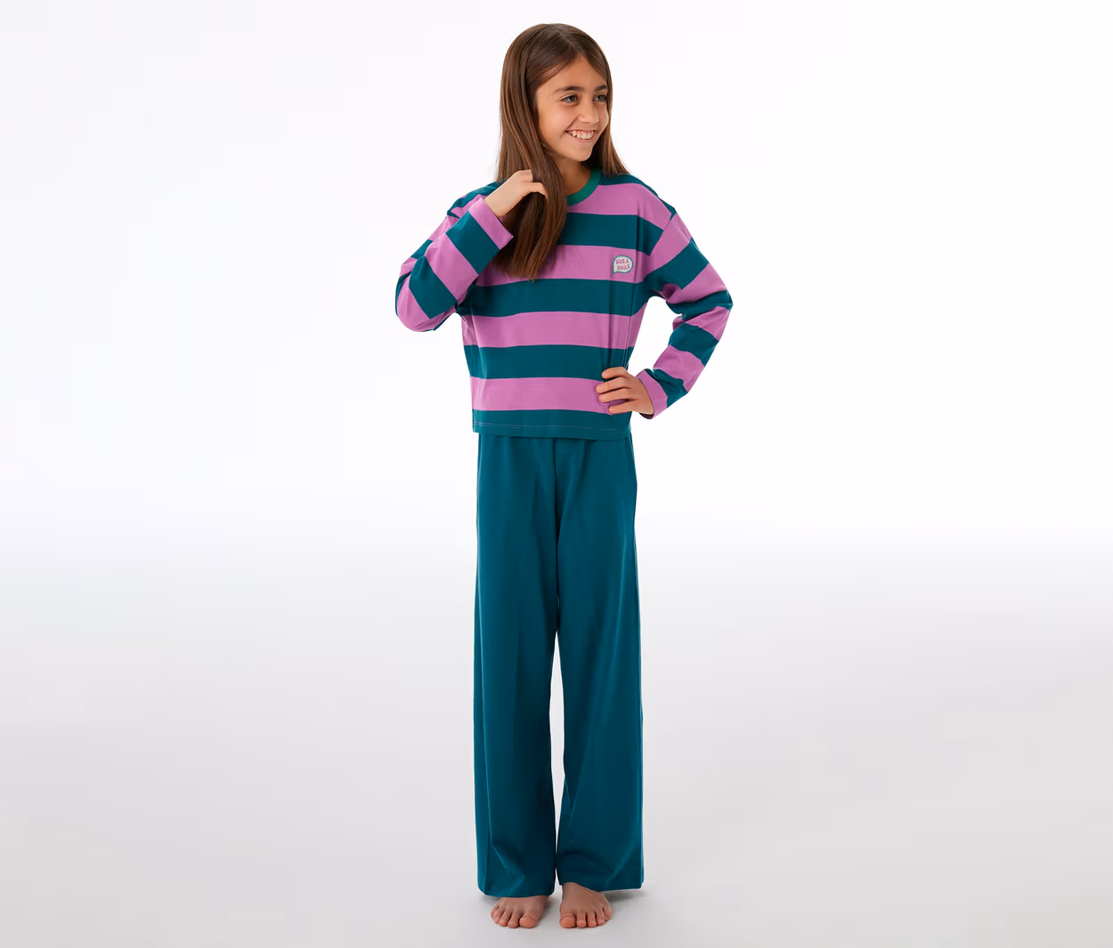Lächelndes Mädchen in einem SCHIESSER Kinder-Pyjama mit lila-grün gestreiftem Oberteil und grüner Hose.