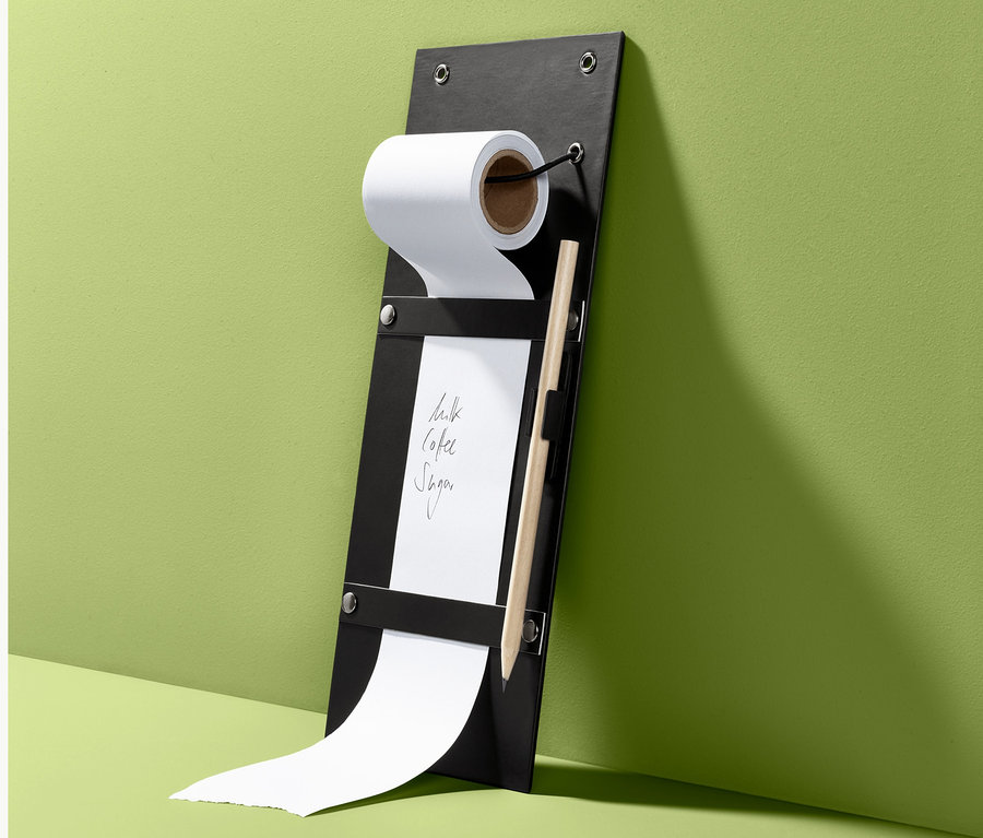Ein Notizrollenhalter in Schwarz mit Papierrolle, Bleistift und der Aufschrift Milch, Kaffee, Zucker.