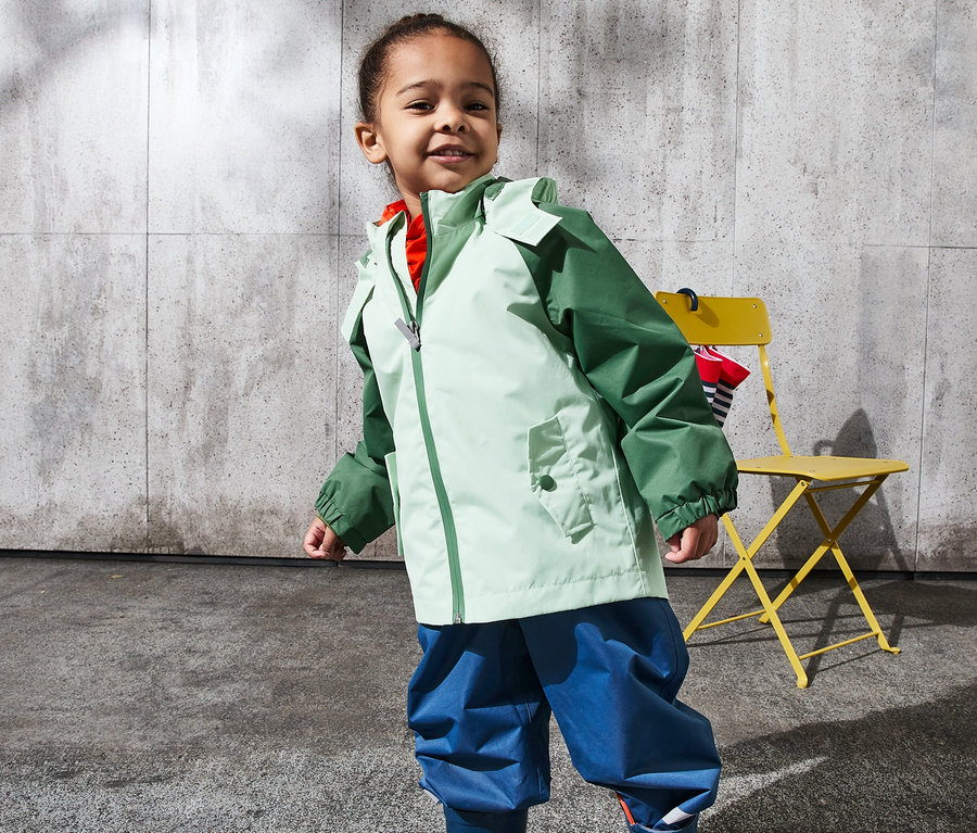 Mädchen posiert in hellgrün-dunkelgrüner Regenjacke aus recyceltem Material.
