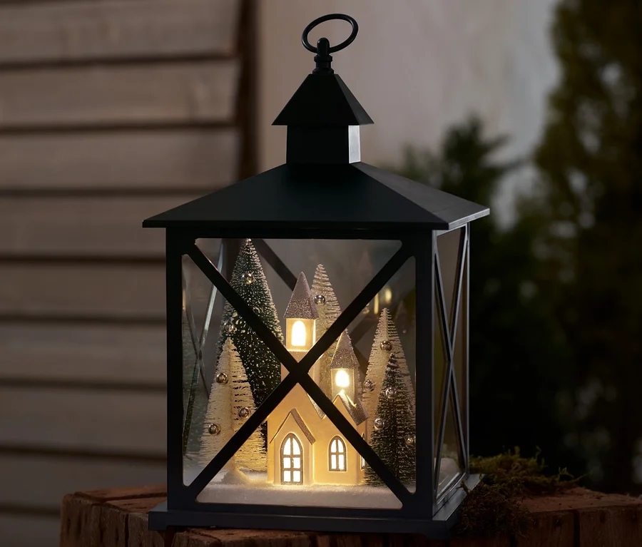 Eine LED-Dekolaterne mit Winterwald-Motiv steht auf einer Holzoberfläche.
