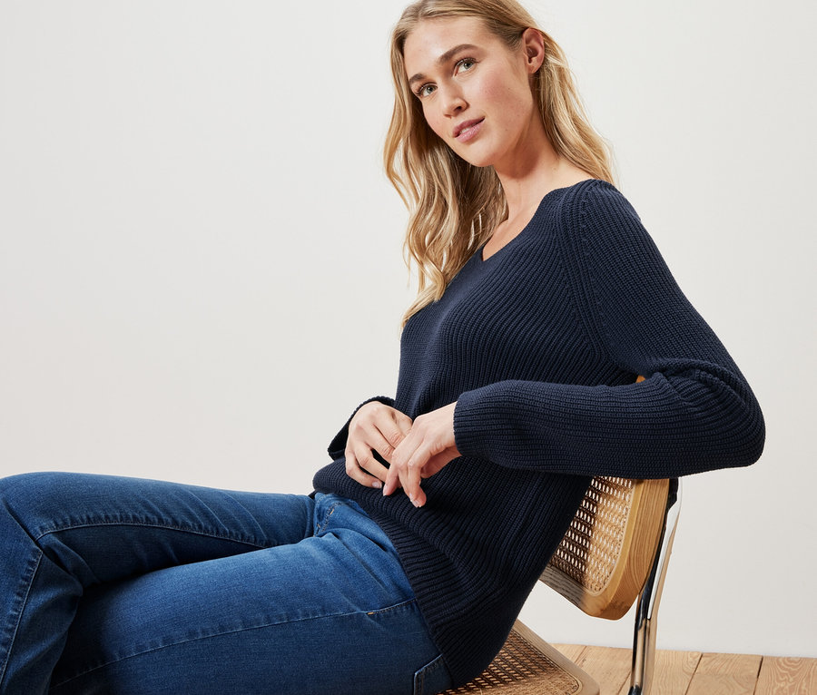 Frau sitzt auf einem Stuhl und trägt einen dunkelblauen Strickpullover.