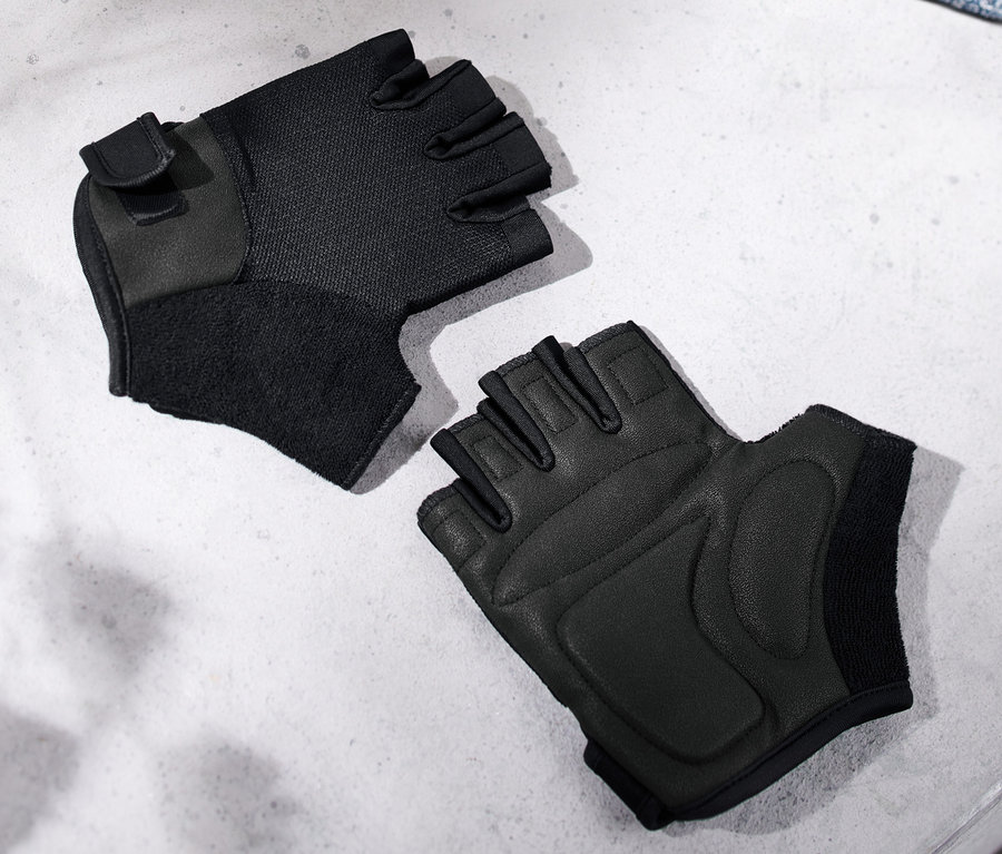 Zwei schwarze Fitness-Handschuhe liegen auf einer grauen Bank neben einem blauen Handtuch.