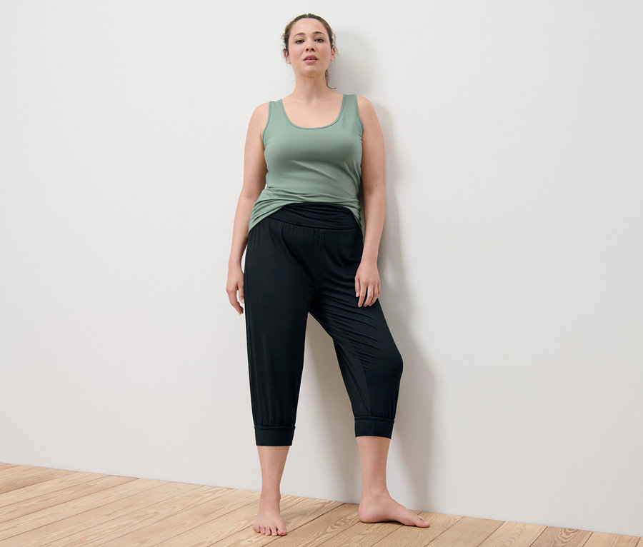 Frau posiert in grünem Top und schwarzer 3/4-Yogahose.